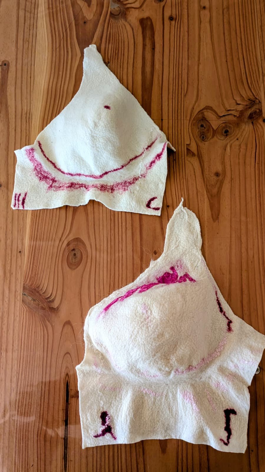 Deux gabarits mono-seins en laine feutrée, tracés à l'encre rose, posés sur une table en bois